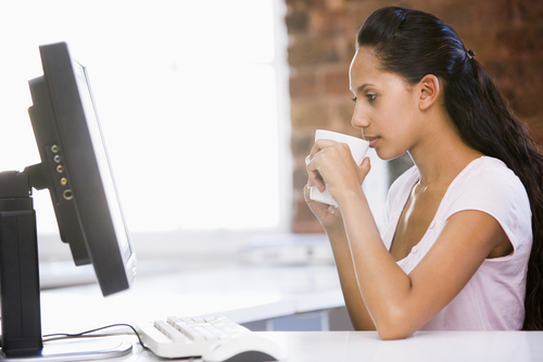 Businesswoman in office drinking coffee and looking at computer